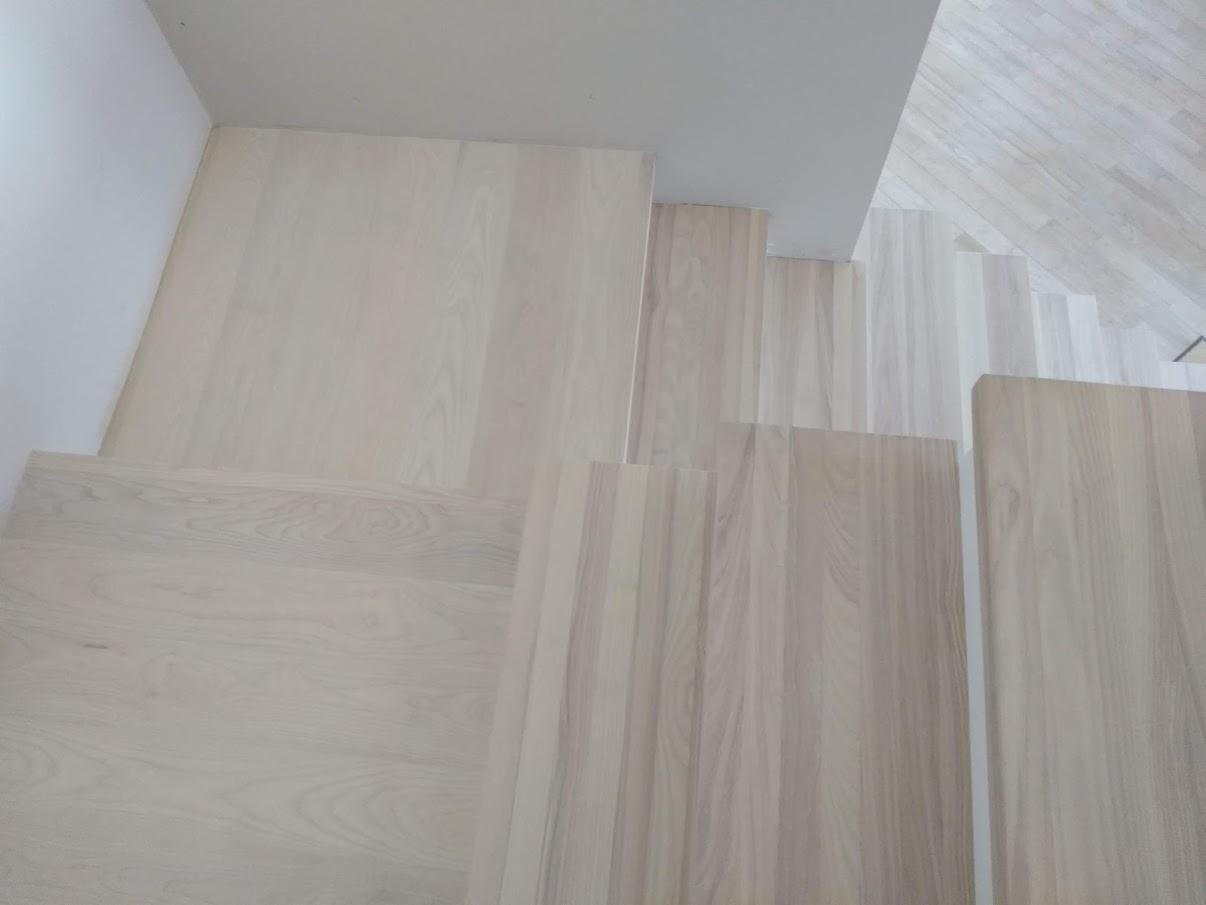 Jasne, drewniane schody widziane z góry, z delikatnym usłojeniem i minimalistycznym wykończeniem.