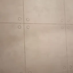 Ściana z szarych płyt imitujących beton, z widocznymi okrągłymi wgłębieniami w rogach każdej płyty, tworzącymi regularny wz&oacute;r.