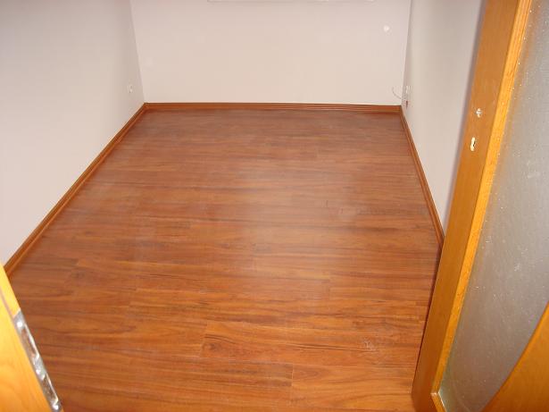 Pokój z nowo ułożoną podłogą z paneli o ciepłym, brązowym odcieniu drewna, widoczne listwy przypodłogowe i fragment drzwi z szybą.