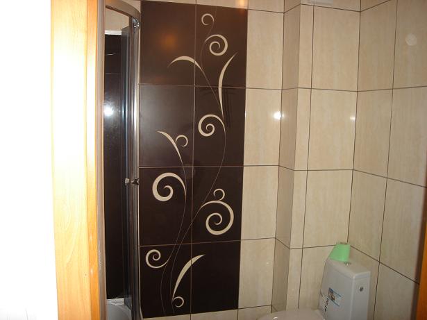 Wykończona łazienka z kabiną prysznicową i toaletą, ściany wyłożone brązowymi i beżowymi płytkami z dekoracyjnym motywem roślinnym.