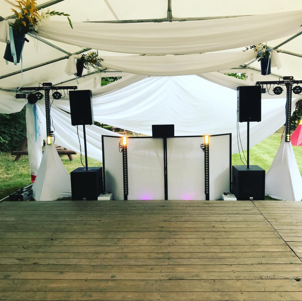 Scena z nagłośnieniem i oświetleniem pod białym namiotem udekorowanym kwiatami, przygotowana na imprezę.