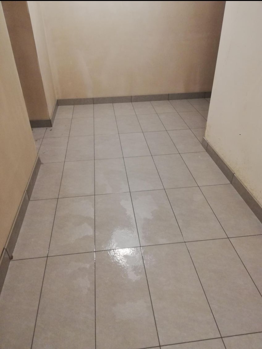 Wykończone wnętrze: beżowe płytki podłogowe z szarą listwą przypodłogową w korytarzu o kremowych ścianach. Widok na świeżo położoną podłogę.