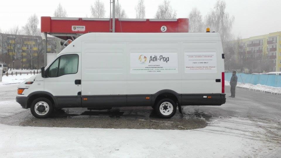 Biały samochód dostawczy firmy Adi-Pop zaparkowany w zimowej scenerii na tle budynku, z widocznym logo i numerem telefonu na boku.