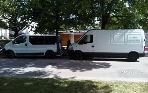 Dwa białe busy o różnych rozmiarach zaparkowane obok siebie na ulicy w słoneczny dzień, z drzewami w tle.