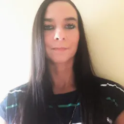 Portret kobiety z długimi, ciemnymi włosami, ubranej w koszulkę w paski, na jednolitym, jasnym tle. Widoczne delikatne cienie modelujące twarz.