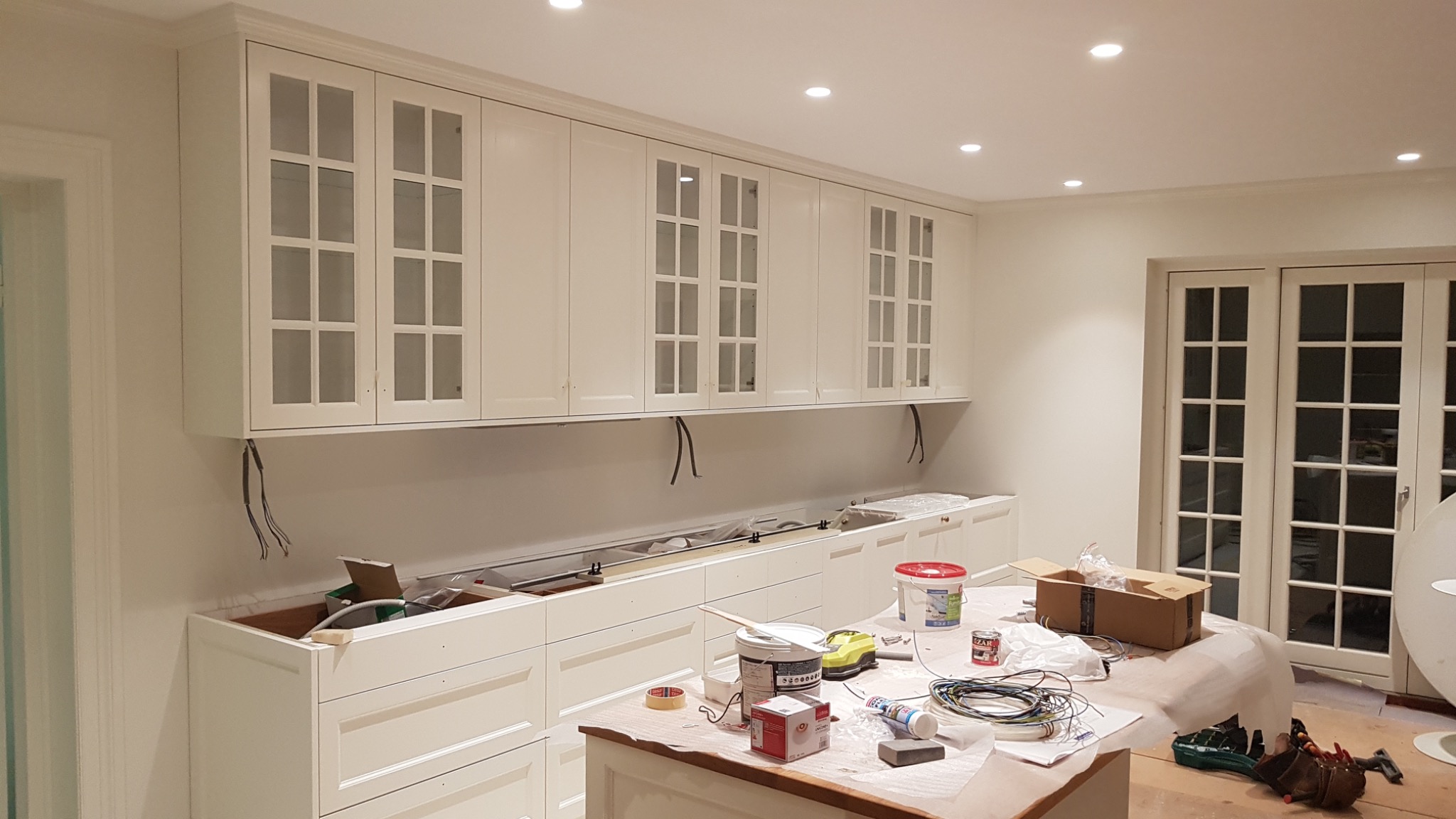 Montaż białych, przeszklonych szafek kuchennych w Tarnobrzegu, widoczne przewody elektryczne i narzędzia na blacie, sugerujące trwające prace wykończeniowe.