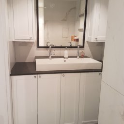 Marzena Camila Wojtkiewicz GREEN-ARTE pracownia wnętrz i malarstwa - Nowoczesna łazienka z białą szafką pod umywalką, czarnym blatem i dużym lustrem w czarnej ramie. Widoczne baterie umywalkowe i marmurowe płytki na ścianach.