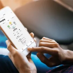 Kobieta przegląda aplikację mobilną z interfejsem monitoringu instalacji OZE, widoczne dane o ładowaniu i ikonki paneli słonecznych.