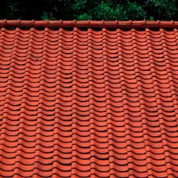 Nowy, ceramiczny dach w odcieniach czerwieni, z widoczną fakturą dachówek i zielenią drzew w tle.