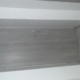 Szary panel ścienny z ukrytymi drzwiczkami rewizyjnymi, zamontowany w Gryfowie Śląskim, z widocznymi fragmentami białych ścian i paneli podłogowych.