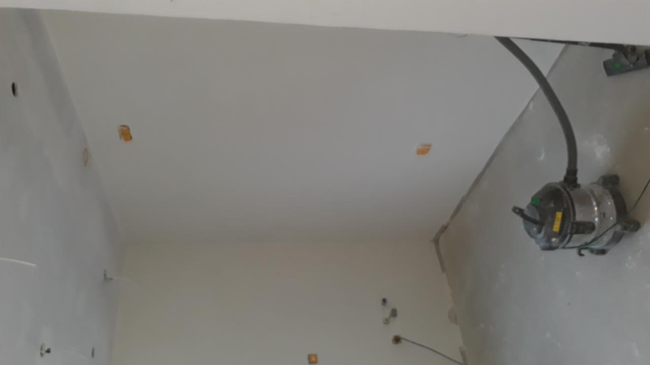 Pokój w trakcie prac wykończeniowych, widoczna gładka, biała ściana i sufit z przygotowanymi otworami na gniazdka elektryczne oraz szlifierka do gładzi z odkurzaczem.