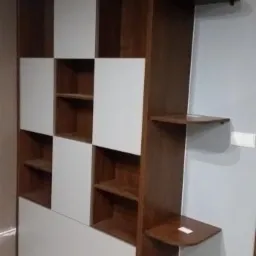 Brązowo-biały regał z półkami i szafkami, z dodatkowymi półkami bocznymi przymocowanymi do ściany.