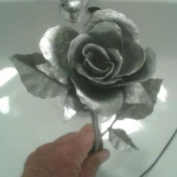 PHU TEGOLA Bartosz Wąsik - Ręcznie wykonana metalowa róża w odcieniach szarości, trzymana w dłoni na tle białej umywalki.