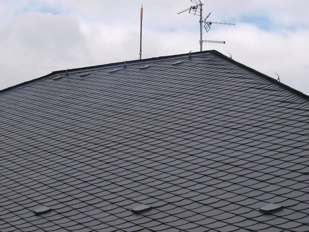 Nowy dach z łupka w Szczecinie, widok z dołu, z anteną telewizyjną i odgromnikiem w tle na tle pochmurnego nieba.