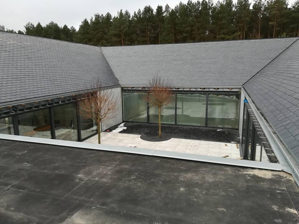 Nowoczesny dom z szarym dachem łupkowym, widok z góry na rynny i wewnętrzny dziedziniec z dwoma małymi drzewkami.