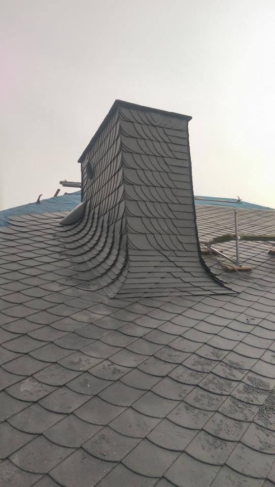 Dach pokryty łupkiem z kominem również wykończonym łupkiem, z widocznym rusztowaniem w tle.