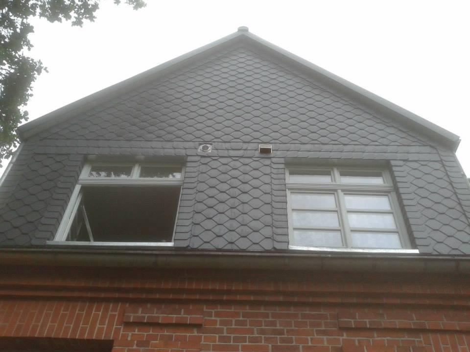 Szary dach z łupka z dwoma oknami, jedno otwarte, na tle ceglanej ściany.