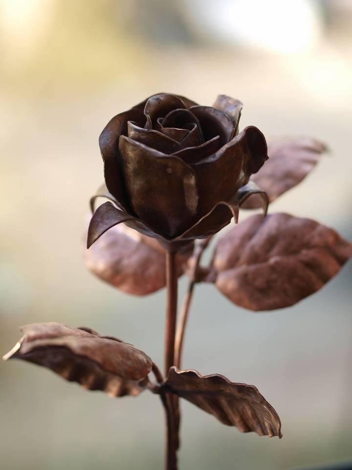 Miedziana róża z metalu, ręcznie wykonana, z widocznymi śladami obróbki i patyną, na rozmytym tle.