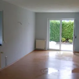 Pusty pokój z oknem z roletami zewnętrznymi, przesuwanymi drzwiami balkonowymi i błyszczącą podłogą, gotowy do remontu lub umeblowania.