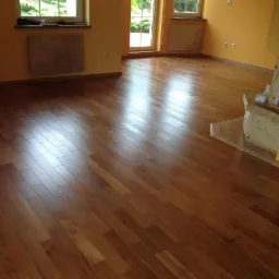 Wykończona podłoga z parkietu ułożonego w cegiełkę w jasnym pokoju z żółtymi ścianami i marmurowym obramowaniem kominka.