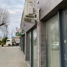 Zewnętrzna jednostka klimatyzacyjna zamontowana na ścianie budynku z kamienną elewacją, widoczne przewody w białej listwie, na chodniku zaparkowany samoch&oacute;d ciężarowy