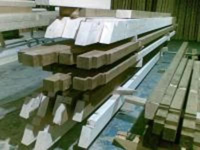 Stosy surowej więźby dachowej z jasnego i ciemnego drewna ułożone w hali magazynowej.