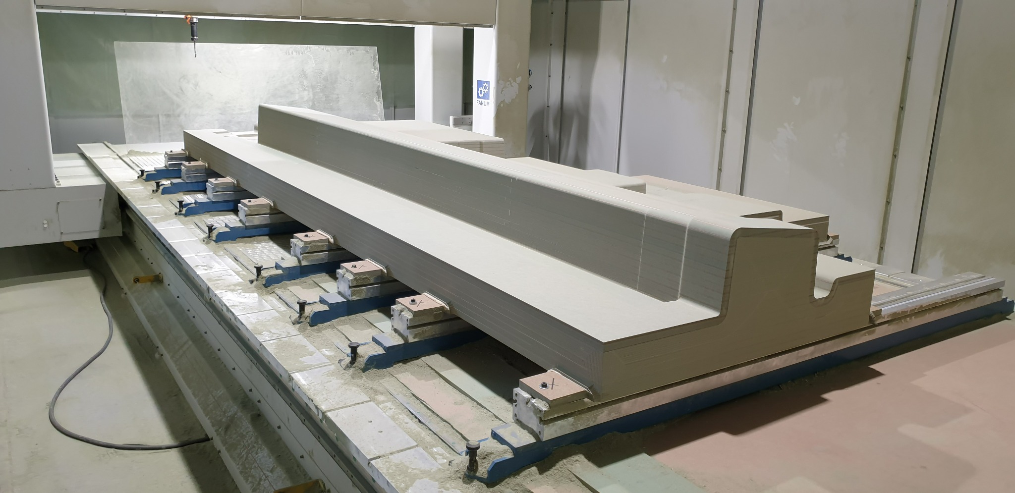 Obrabiany element z płyty drewnopochodnej na stole frezarki CNC 5-osiowej, widoczne mocowania i ślady obróbki.