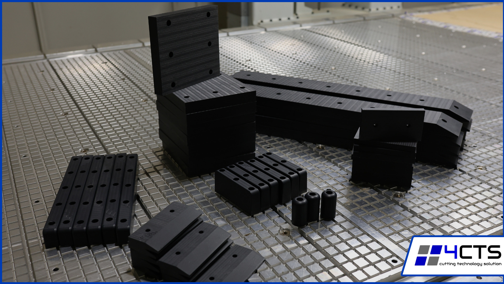 Czarne elementy z otworami ułożone na metalowej siatce, prawdopodobnie wykonane metodą CNC. Widoczne różne kształty i rozmiary, sugerujące precyzyjną obróbkę.