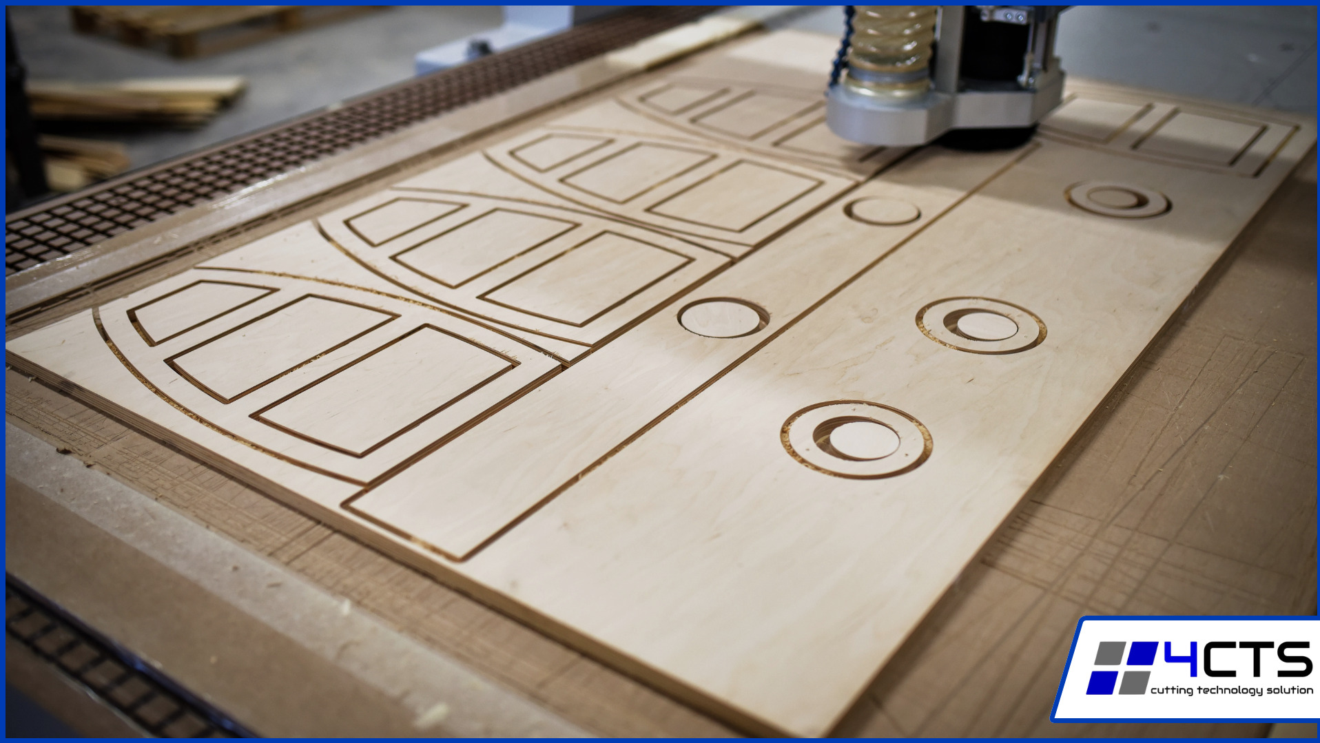 Frezowanie CNC w jasnej płycie drewnianej. Widoczne wyfrezowane wzory geometryczne i okrągłe otwory. Maszyna CNC w górnej części kadru.