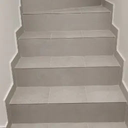 Schody wyłożone szarymi płytkami ceramicznymi z białymi listwami przypodłogowymi, widok z dołu.