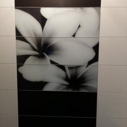 OPALIŃSKI Nowoczesne Wykończenia - Ściana wyłożona białymi i czarnymi płytkami ceramicznymi, z centralnym pasem płytek z motywem kwiatowym w odcieniach szarości.