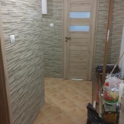 OPALIŃSKI Nowoczesne Wykończenia - Ukończona łazienka w Nowej Sarzynie z beżowymi płytkami imitującymi kamień na ścianach i podłodze, widoczna drewniana ościeżnica drzwi z szybami i narzędzia pracy w rogu.