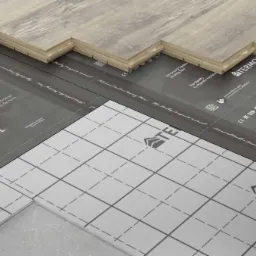 Układanie drewnopodobnych paneli podłogowych na folii grzewczej z nadrukowanymi logotypami producentów.