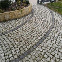 Q.MAN Dariusz Prandzioch - Ułożona kostka granitowa w kształcie łuku prowadząca do bramy wjazdowej, z widocznym obrzeżem rabaty kwiatowej.