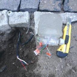 Q.MAN Dariusz Prandzioch - Przygotowanie do podłączenia oświetlenia w kostce granitowej: widoczne kable, złączki WAGO, nóż monterski i fragment kostki granitowej.