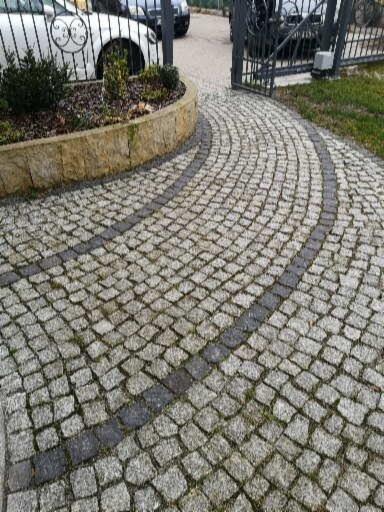 Ułożona kostka granitowa w kształcie łuku prowadząca do bramy wjazdowej, z widocznym obrzeżem rabaty kwiatowej.