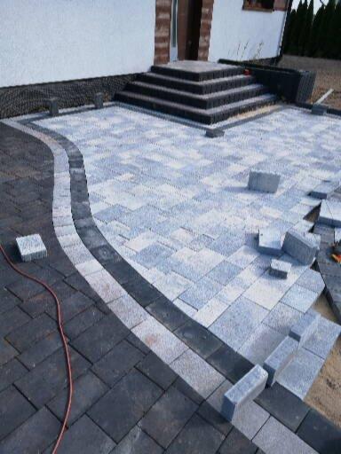 Układanie dwukolorowej kostki brukowej z obrzeżem i schodami wejściowymi do domu.