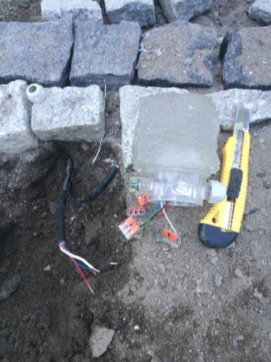 Przygotowanie do podłączenia oświetlenia w kostce granitowej: widoczne kable, złączki WAGO, nóż monterski i fragment kostki granitowej.