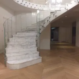 Marmurowe schody z zakrzywioną szklaną balustradą mocowaną punktowo, parkiet ułożony w jodełkę.