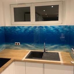 RÓŻYCKI GLASS Grzegorz Różycki - Szklana ściana nad blatem kuchennym z motywem podwodnego krajobrazu, widoczne gniazdka elektryczne i okno w tle.