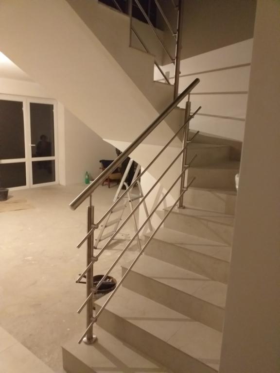 Nowoczesne schody z balustradą ze stali nierdzewnej, widok z dołu, w tle okno i drabina.