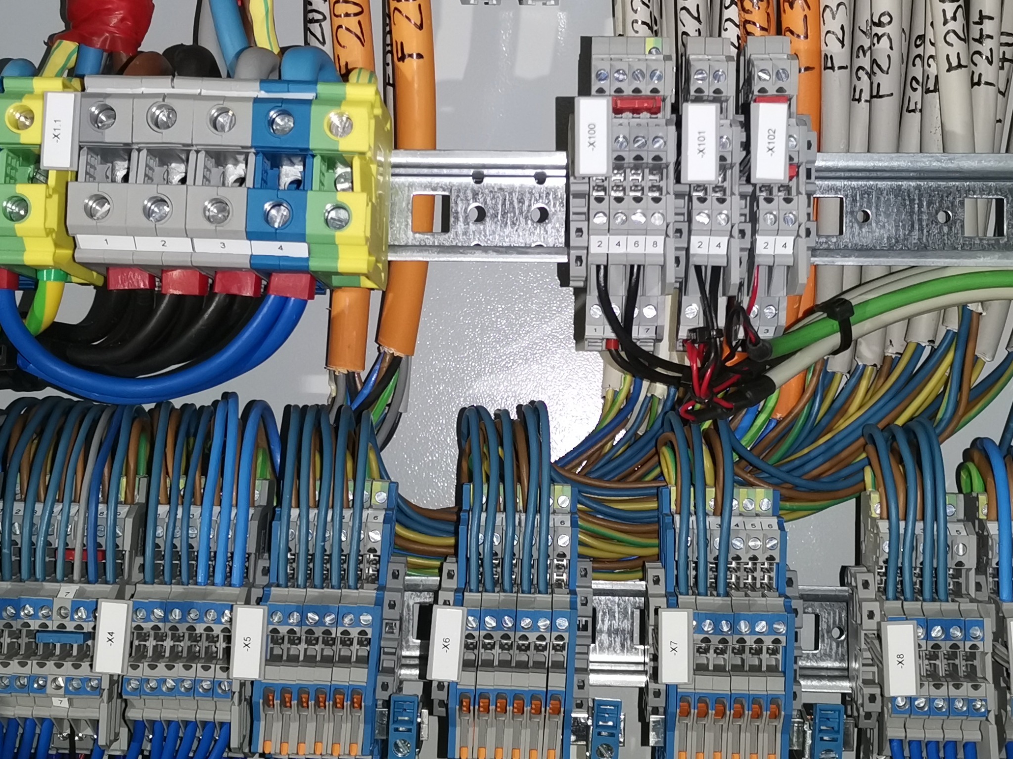 Szczegółowe ujęcie rozdzielnicy elektrycznej z widocznymi listwami zaciskowymi, przewodami o różnych kolorach i oznaczeniach na etykietach, zamontowanymi na szynie DIN wewnątrz szafy sterowniczej.