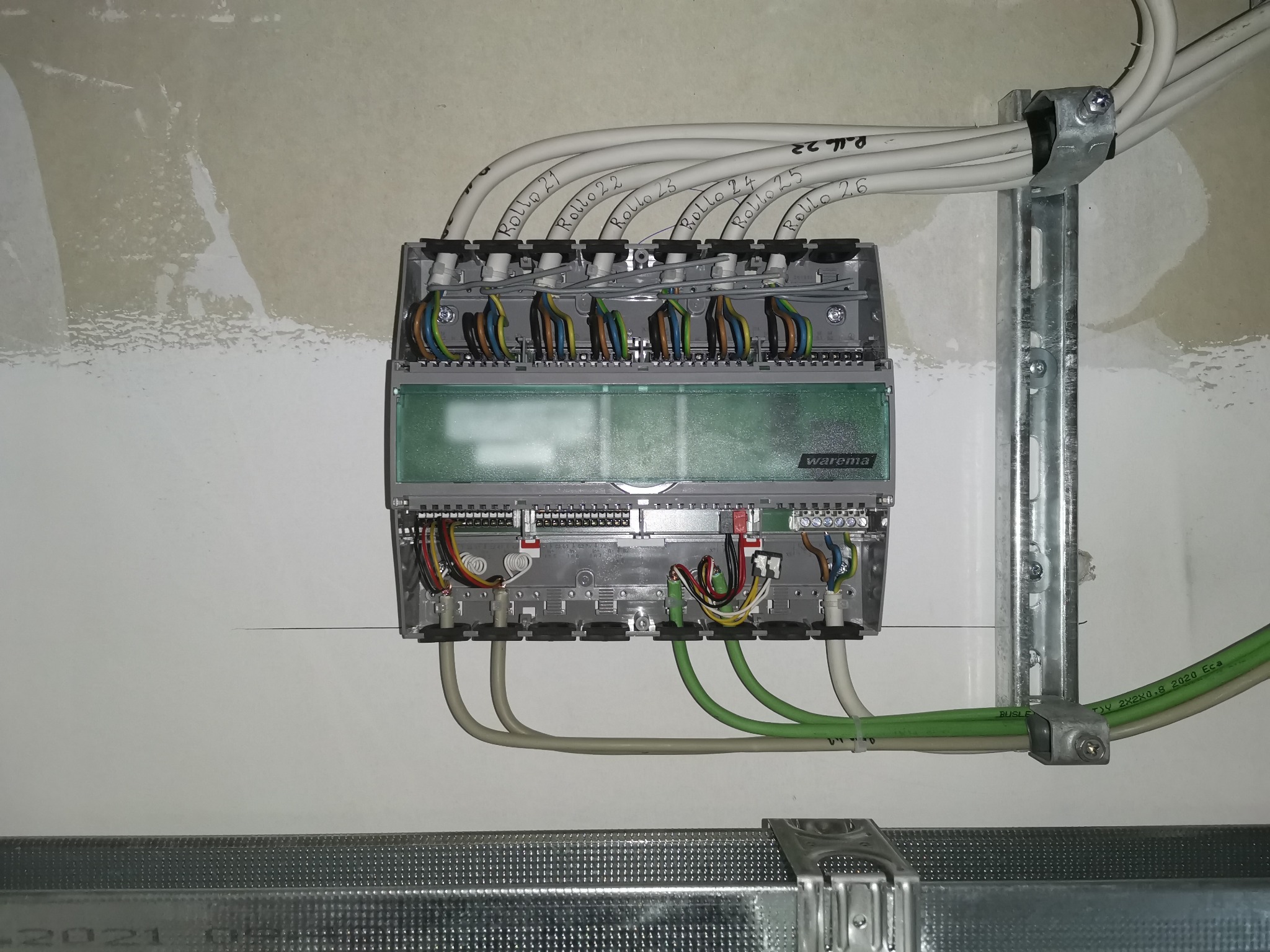 Panel sterowania roletami Warema z podłączonymi przewodami oznaczonymi 'Rollo 21' do 'Rollo 26', zamontowany na ścianie w trakcie prac wykończeniowych.