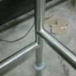 Kamet - Fragment konstrukcji ze stali nierdzewnej, prawdopodobnie poręczy lub balustrady, z widocznym łączeniem rur i elementem mocującym do podłoża, na surowym, betonowym podłożu.