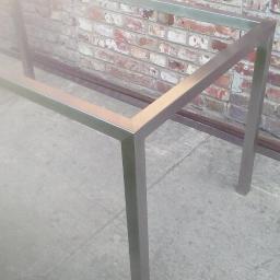 Kamet - Metalowa rama konstrukcyjna w surowym wnętrzu, spawana z profili kwadratowych, widoczna ceglana ściana w tle.