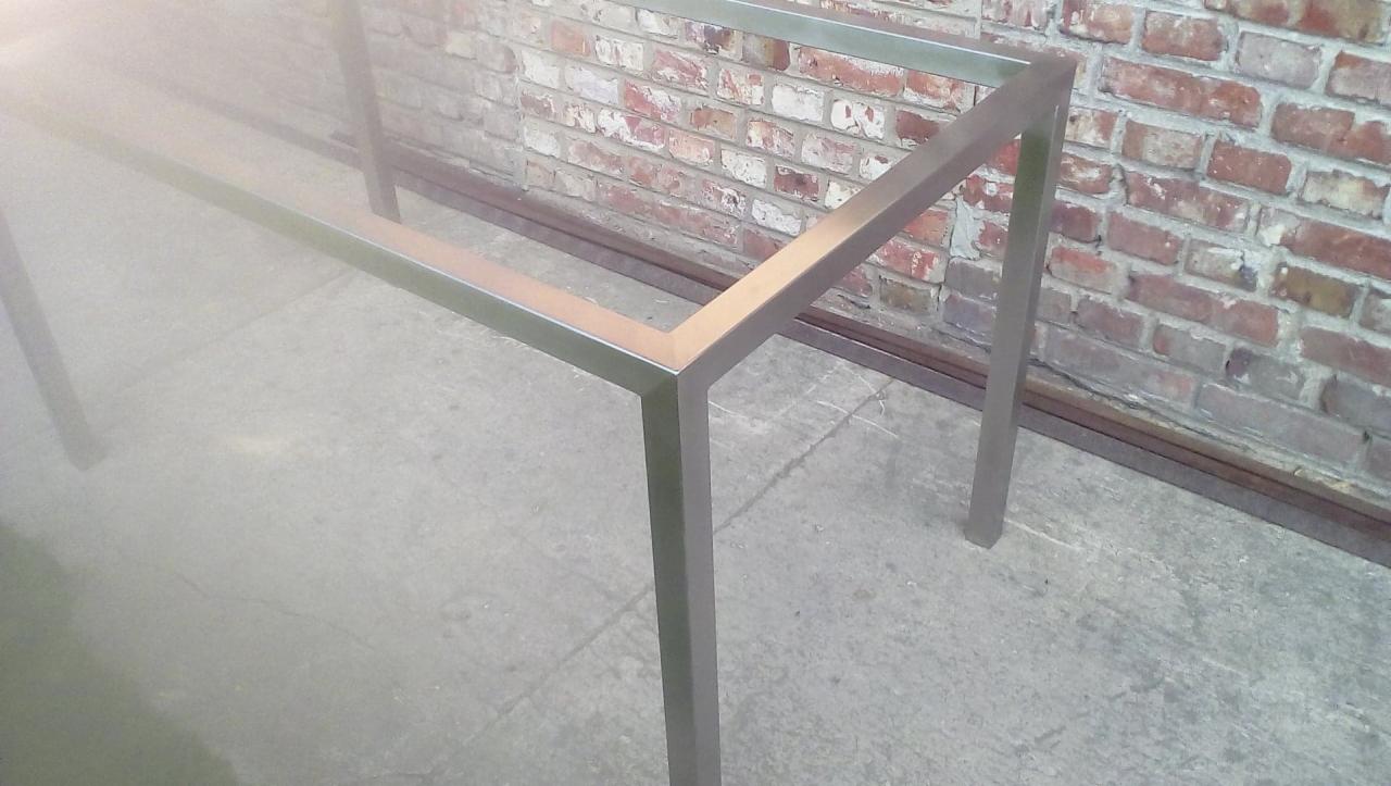 Metalowa rama konstrukcyjna w surowym wnętrzu, spawana z profili kwadratowych, widoczna ceglana ściana w tle.