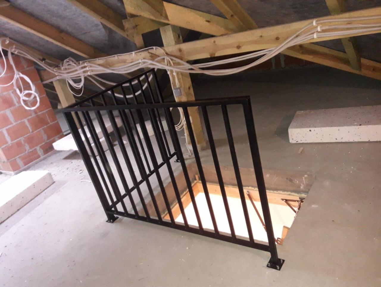 Czarna metalowa balustrada zabezpieczająca otwór w stropie na poddaszu, widok na surowy stan wykończenia, instalacje elektryczne pod sufitem.