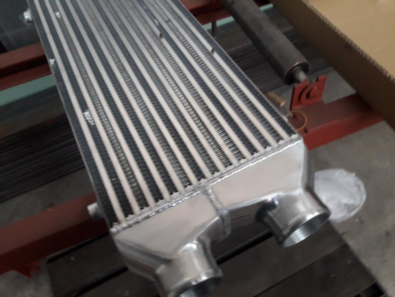 Aluminiowy intercooler z widocznymi spawami na stole warsztatowym, gotowy do montażu.