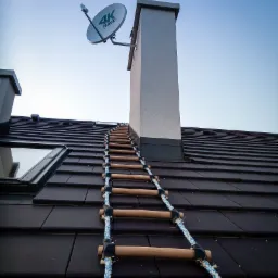 Antena satelitarna Canal+ 4K zamontowana na kominie domu z ciemną dachówką, dostępna po drabinie sznurowej.