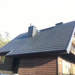 Dom jednorodzinny z ciemną, metalową dachówką modułową i drewnianą elewacją, widok z dołu, z kominem obłożonym tą samą dachówką.